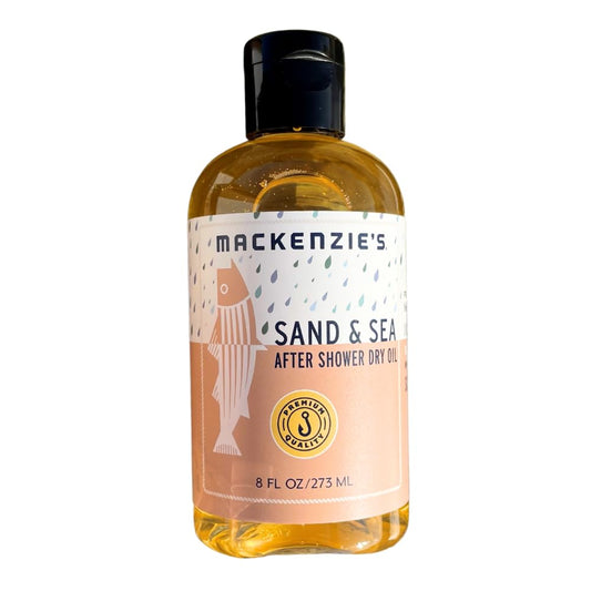MACKENZIE'S Sand & Sea dry oil bottle on sand for post-shower hydration.