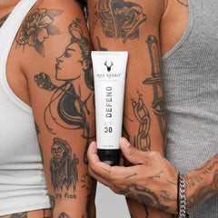 Sunscreen being applied over daily lotion on tattooed skin.