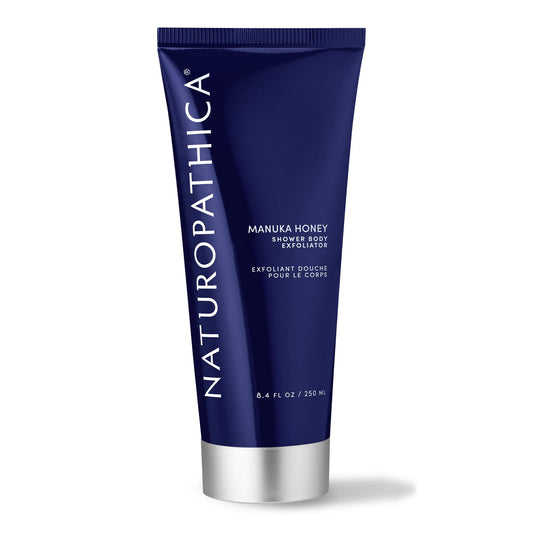 Naturopathica Manuka Honey Shower Body Exfoliator bottle on shelf for hydrating exfoliation.