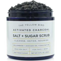 The Yellow Bird activated charcoal scrub jar closeup highlighting natural oils for smooth skin.