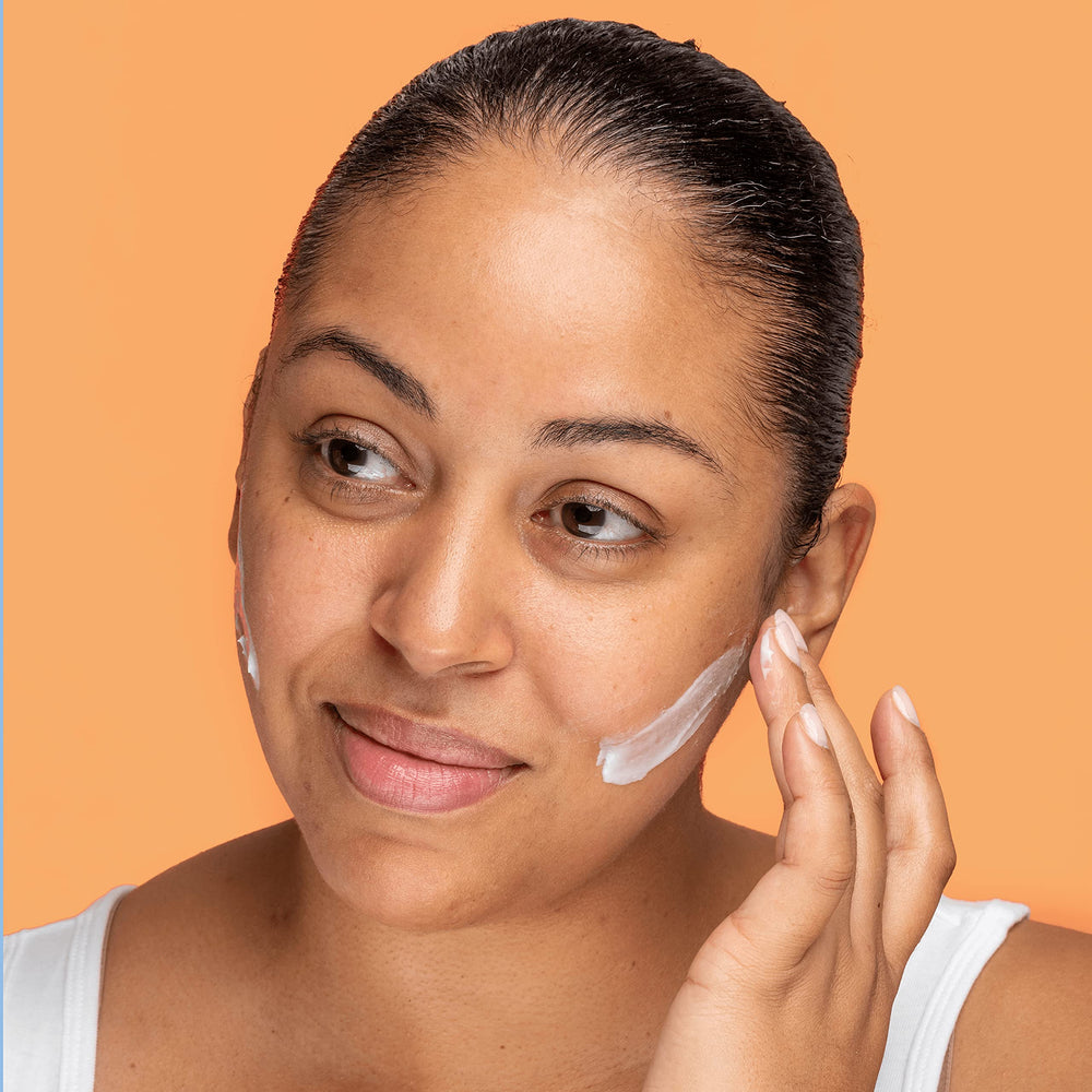 Hands massaging Volition Neroli Complete Creme into the cheeks.