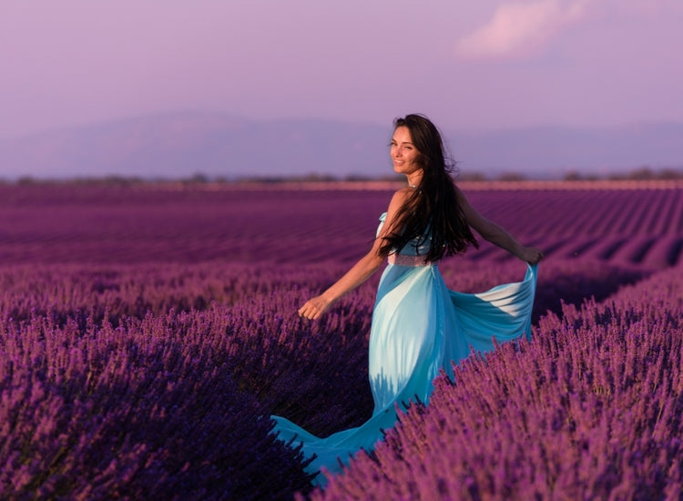 Woman in a blue dress standing in a lavender field with a pink sky.