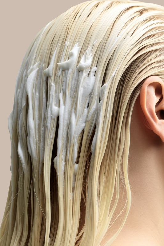 Close-up of a person with blonde hair applying white cream to their scalp.
