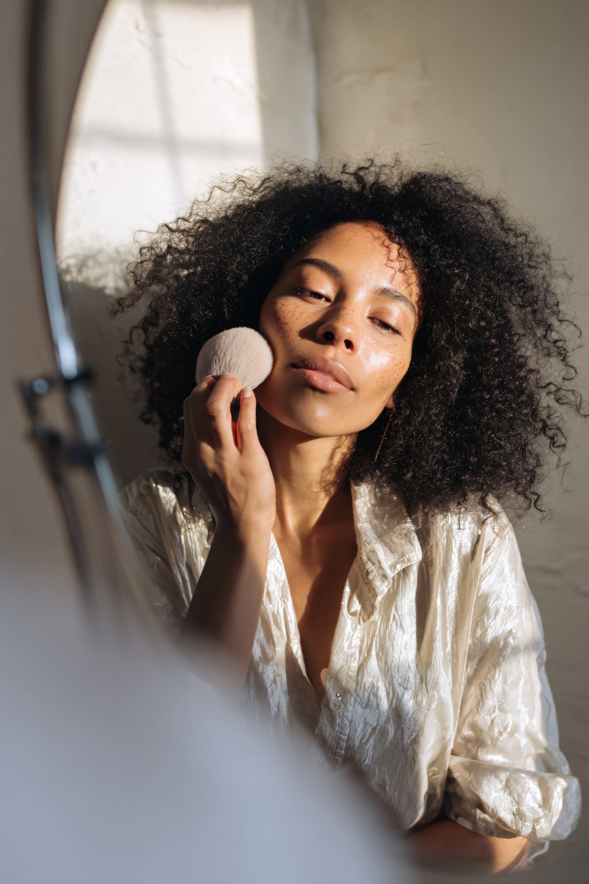 Woman applying makeup with a brush in front of a mirror