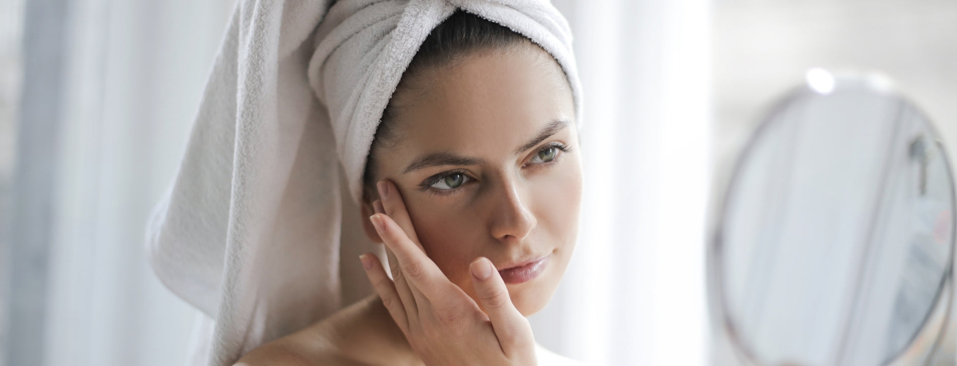 Woman with a towel wrapped around her head looking at herself in the mirror.