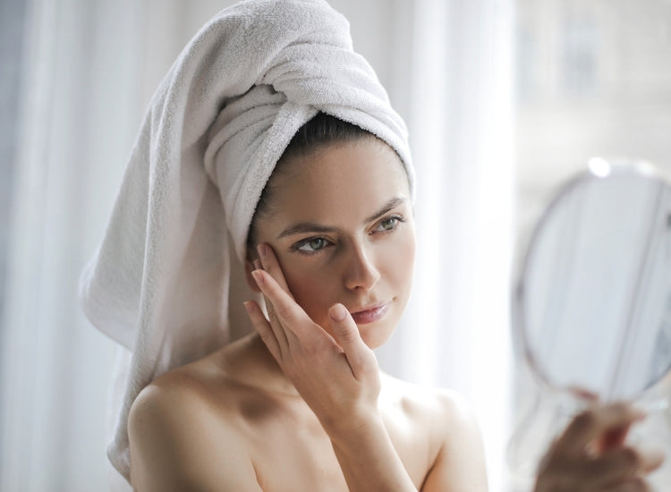 Woman with a towel wrapped around her head looking at herself in a mirror.