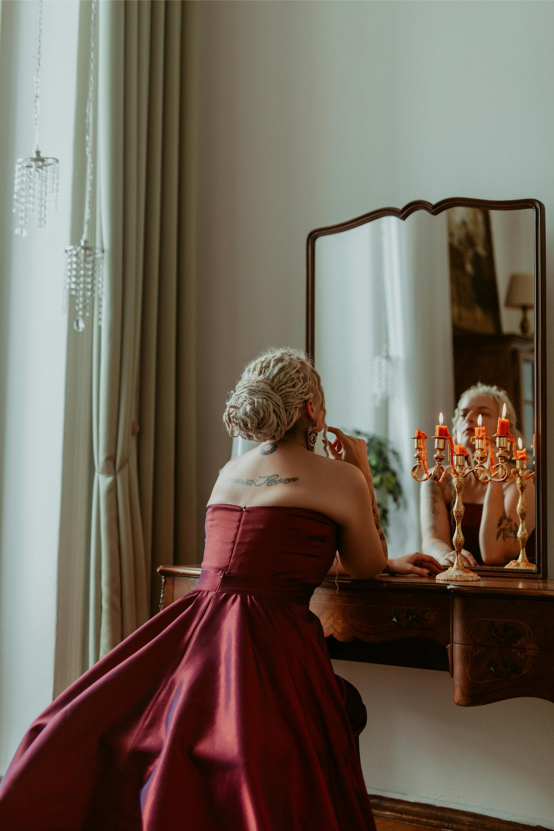 Woman in a red dress adjusting her hair in front of a mirror.