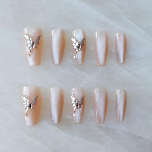 GLORS press-on nails in nude pink with a long ballerina shape and butterfly rhinestones for a luxe look.