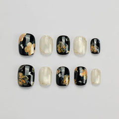 GLORS press-on nails in black with gold flower design for an elegant manicure.