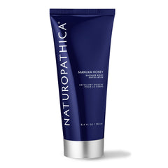Naturopathica Manuka Honey Shower Body Exfoliator bottle on shelf for hydrating exfoliation.