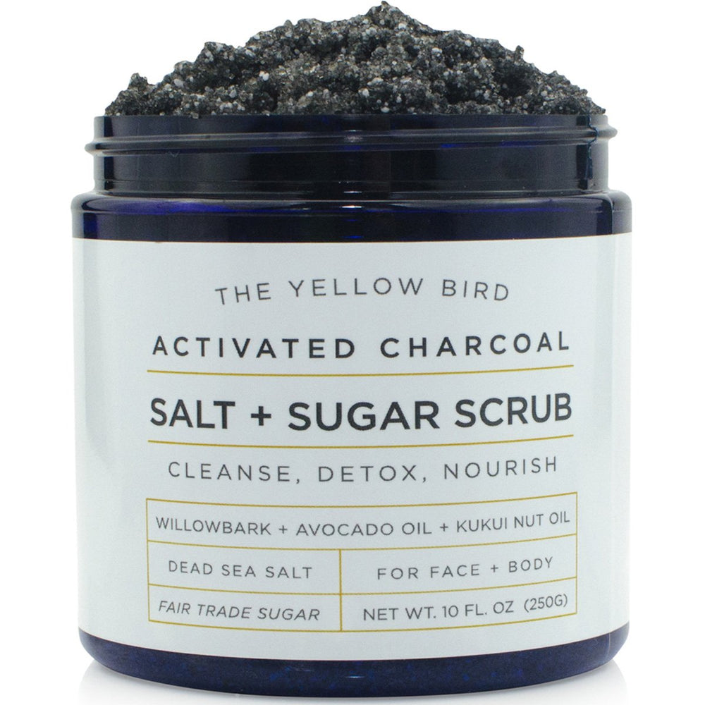 The Yellow Bird activated charcoal scrub jar closeup highlighting natural oils for smooth skin.